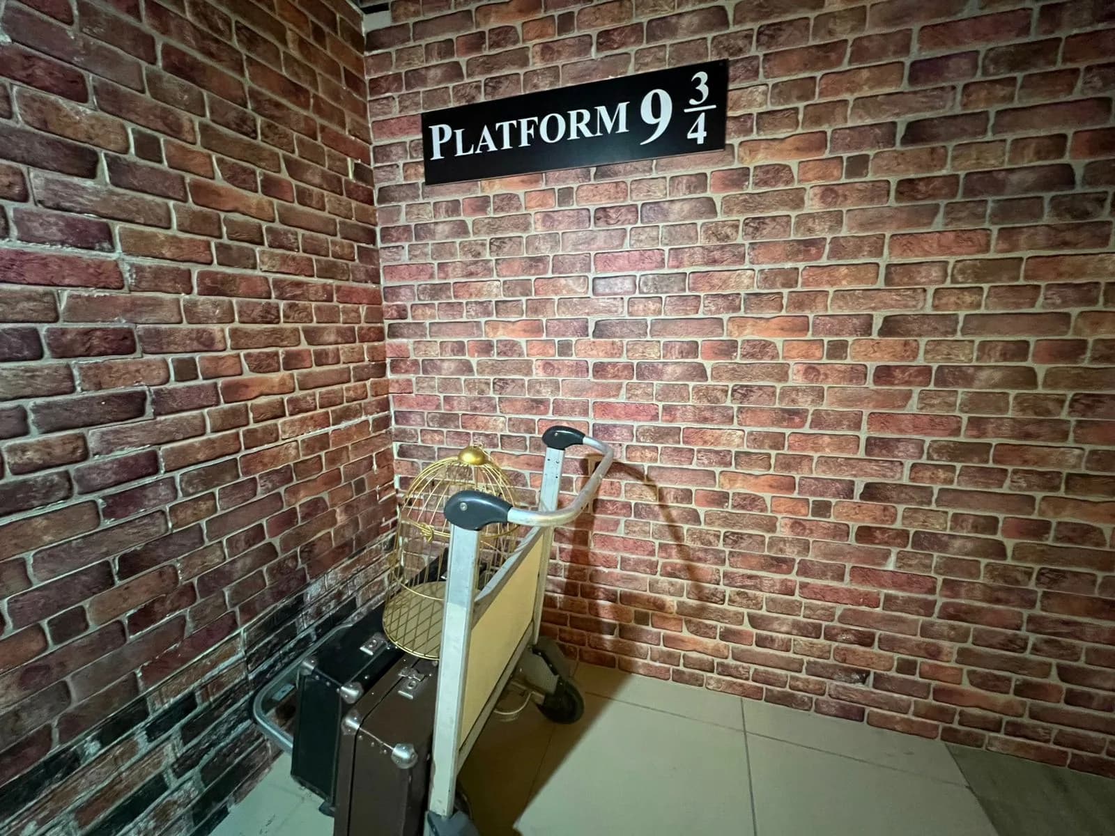 Кирпичная стена с табличкой Platform 9¾ и багажная тележка с чемоданами и золотой клеткой